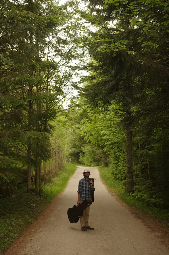 C4C standing on a forest road with a guitar case, reflecting the nature-rooted and acoustic world of Folk-Hop